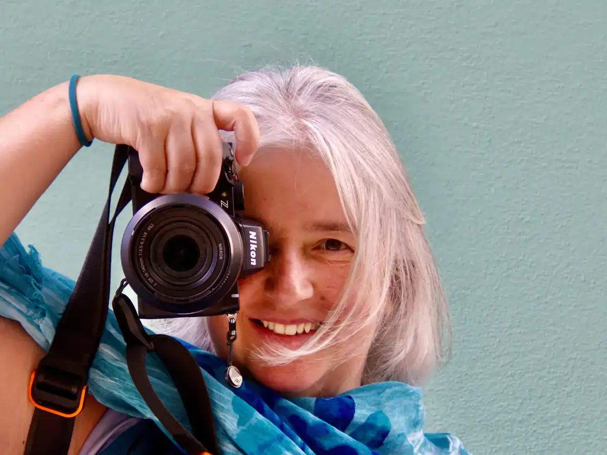 Gianna Gabrielli mentre fotografa con la macchina fotografica, primo piano con sfondo chiaro.